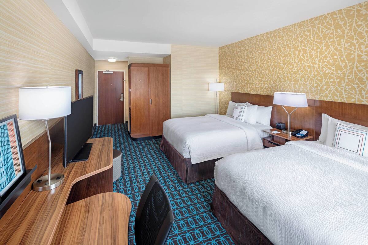 Une chambre d’hôtel avec deux lits, un bureau, une télévision et une porte de salle de bain.