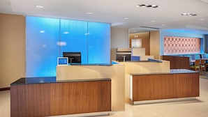 Un área de recepción moderna con mostradores de madera, una pared iluminada en azul y un fondo con diseño.