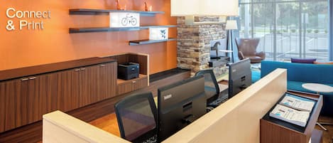 A modern office space with a reception desk, computer workstations, and a seating area with a blue sofa and armchairs.