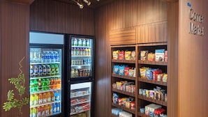 Un mercado de barrio con dispensadores de bebidas refrigeradas y estantes repletos de aperitivos y productos básicos.