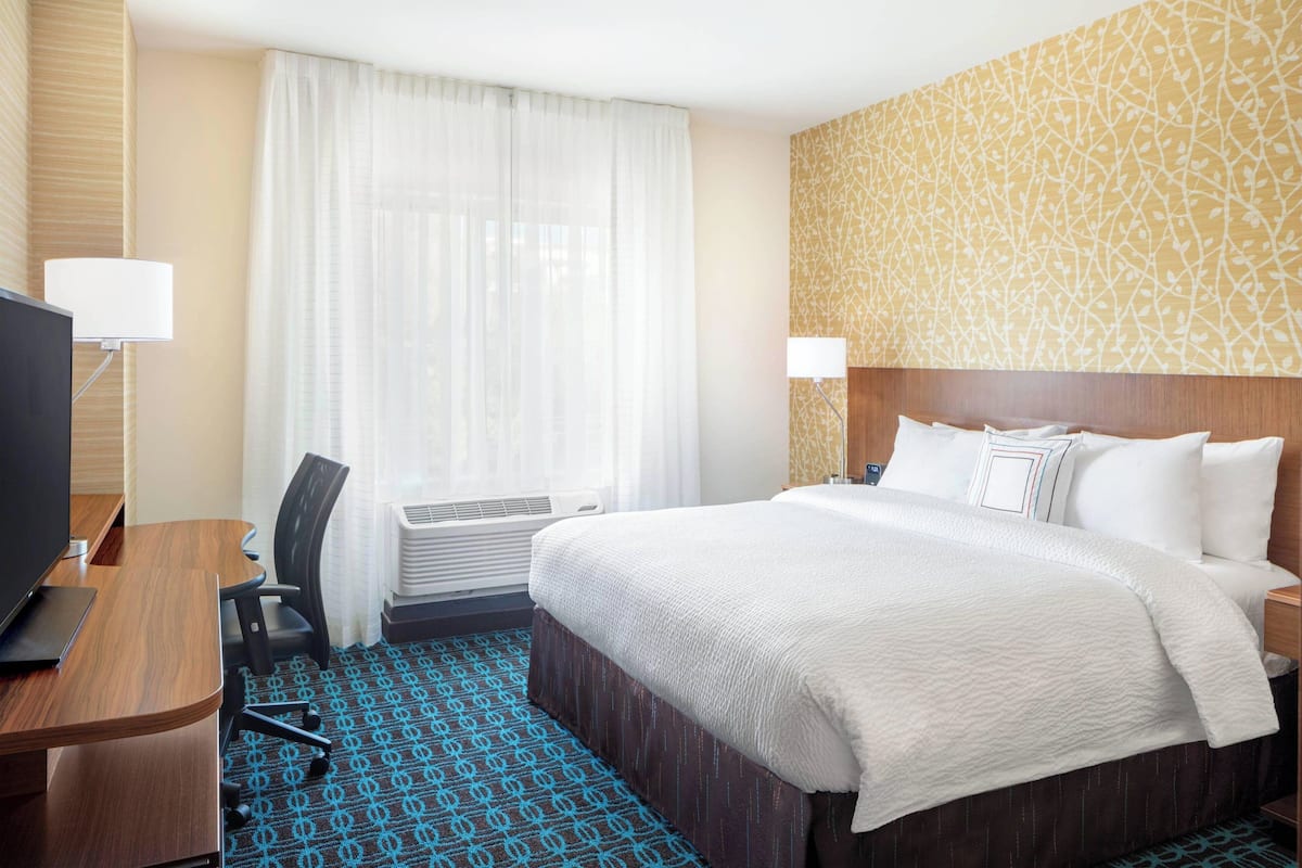 Une chambre d’hôtel avec un lit, un bureau, une télévision et une fenêtre avec des rideaux.