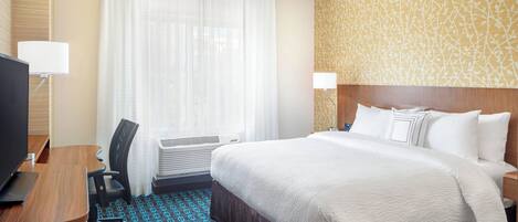 Una habitación de hotel con una cama, un escritorio, un televisor y una ventana con cortinas.
