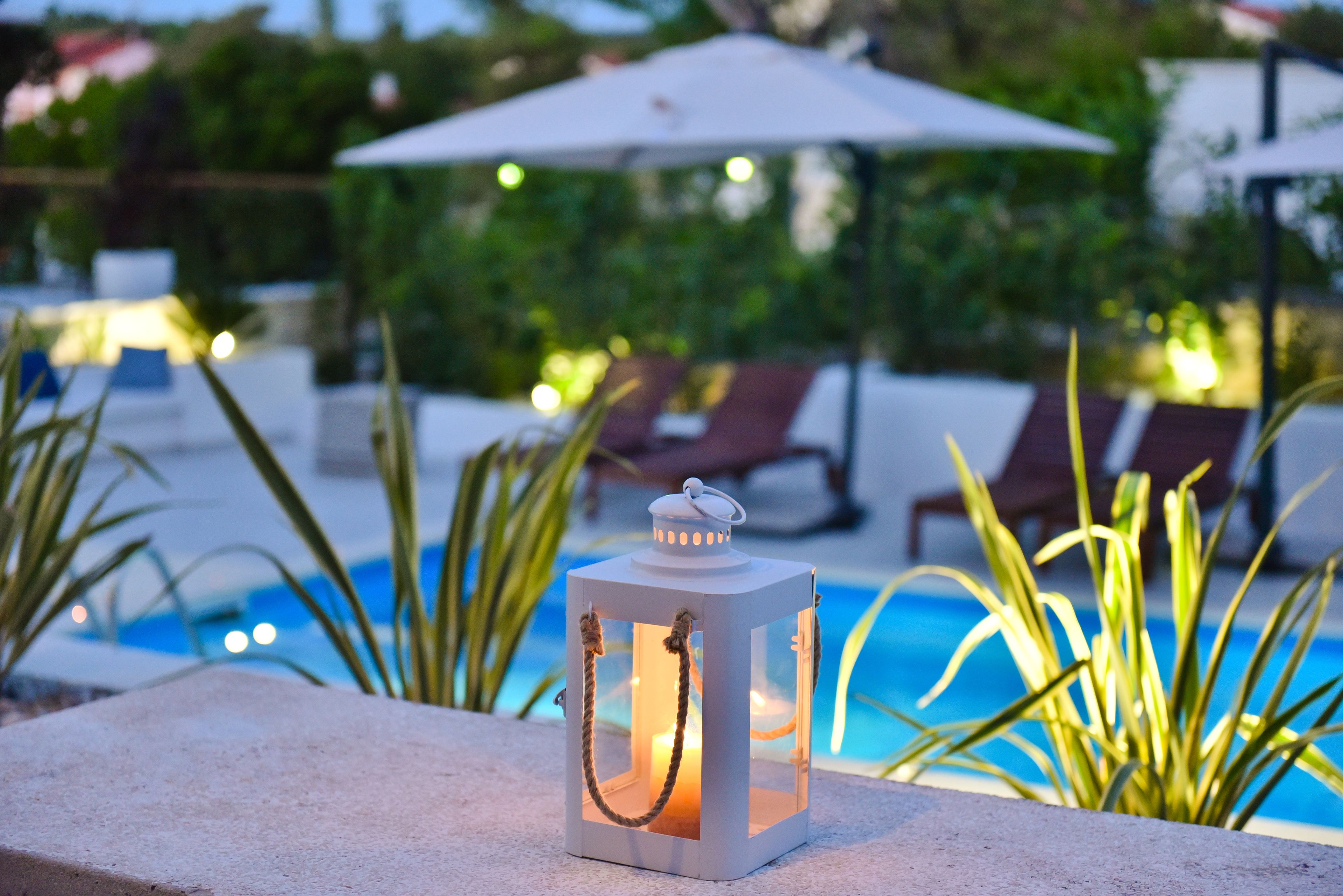 A lantern on a poolside ledge with a pool and lounge chairs in the background.