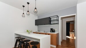 A modern kitchen with a white countertop, black stools, and pendant lighting. - Mediterraneo Garden Apartments (Zadar)