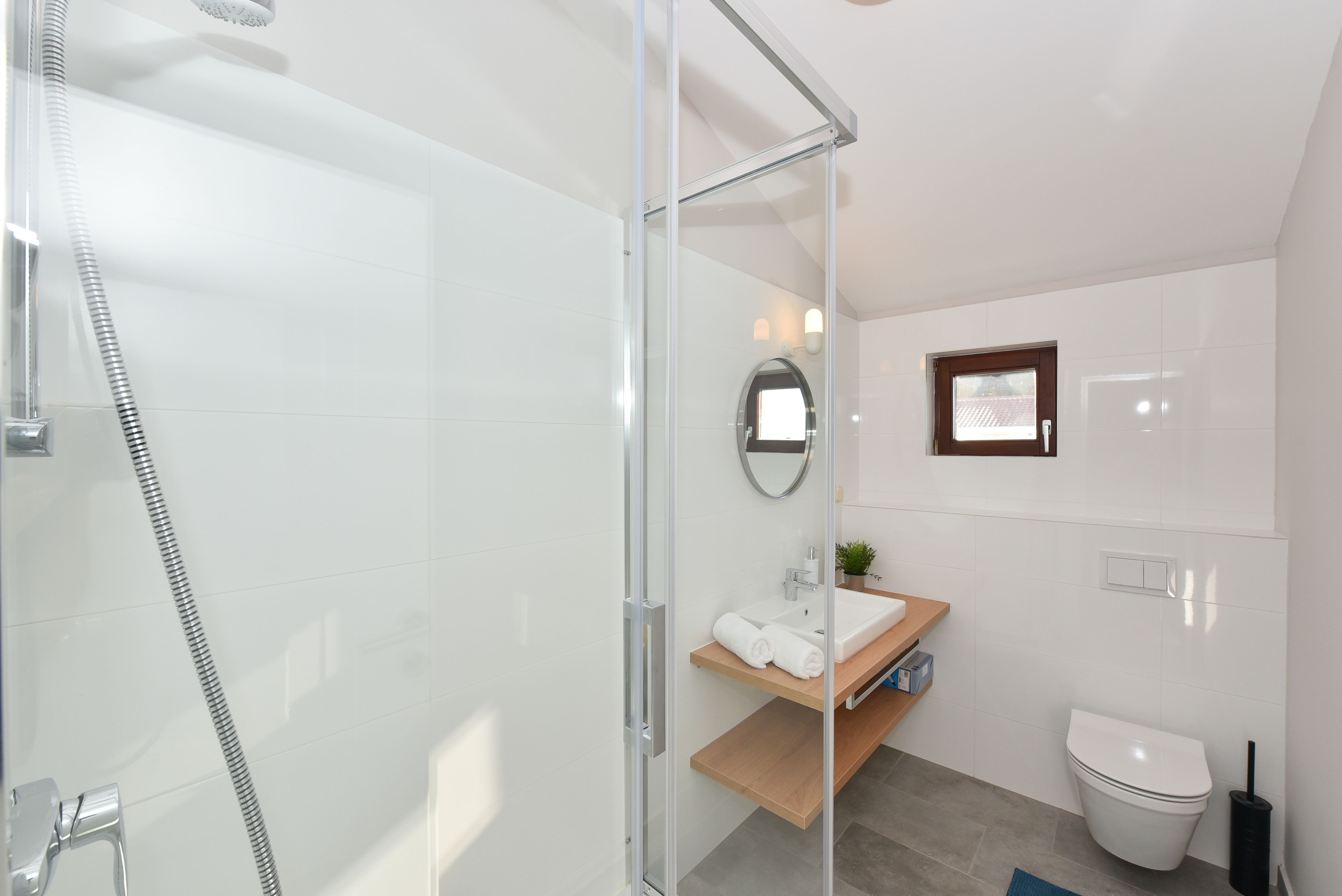 Ein modernes Badezimmer mit Duschkabine aus Glas, einem Holzwaschtisch, einer weißen Toilette und einem kleinen Topfpflanzen.