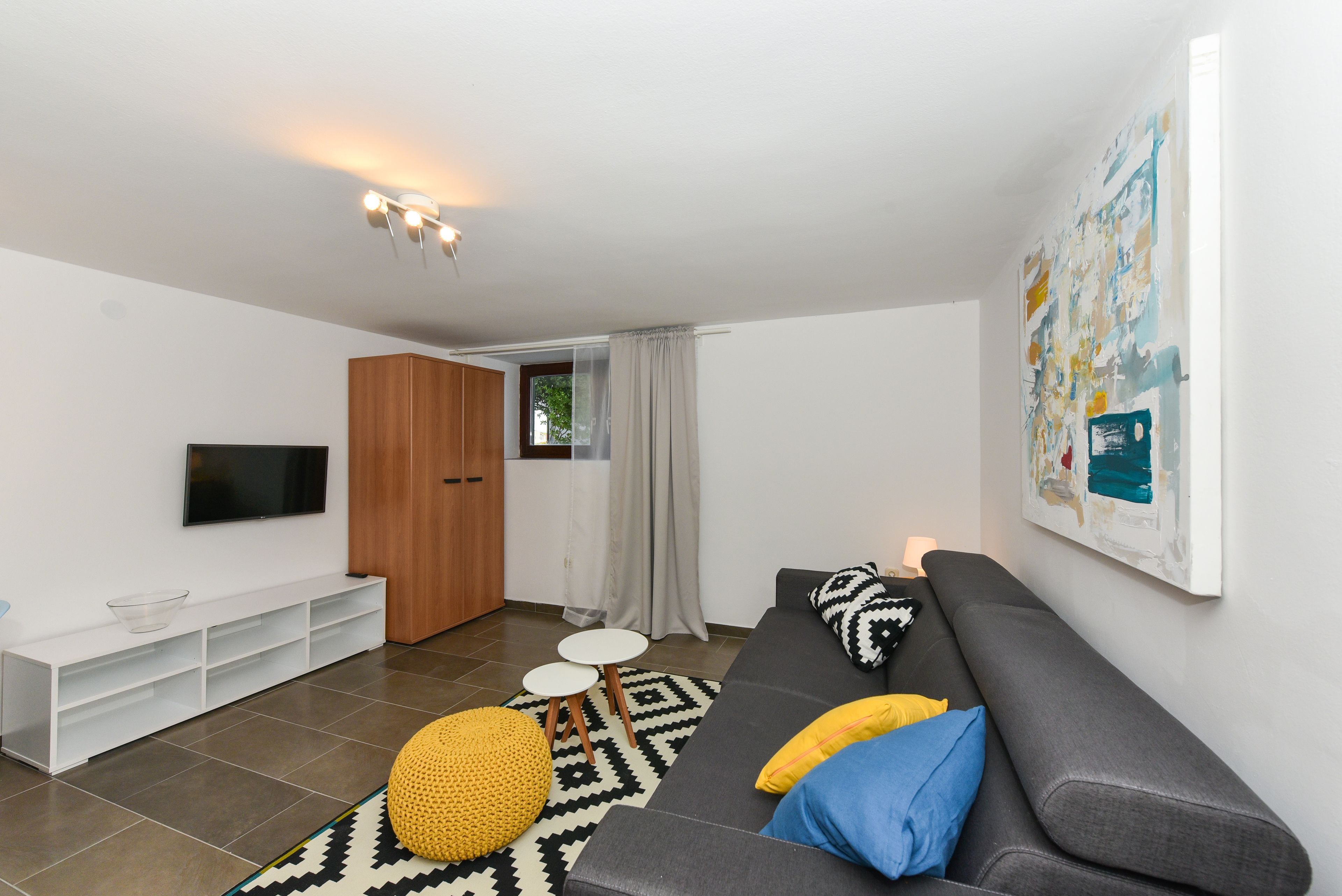 A modern living room with a grey sofa, yellow and blue cushions, a white entertainment unit, and a large abstract painting on the wall.