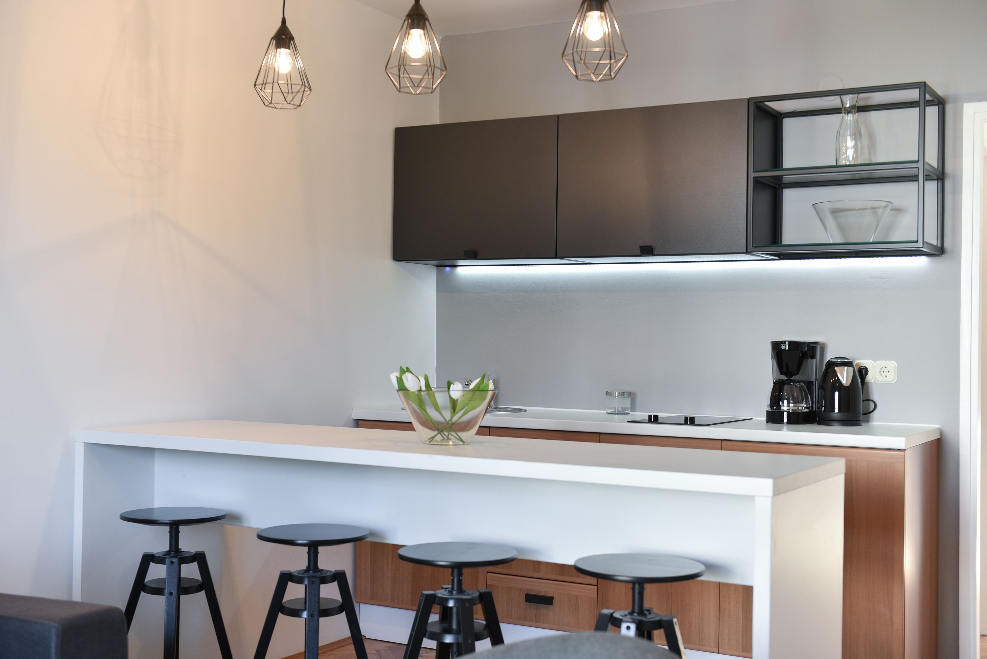 A modern kitchen with a white countertop, three bar stools, and pendant lighting.