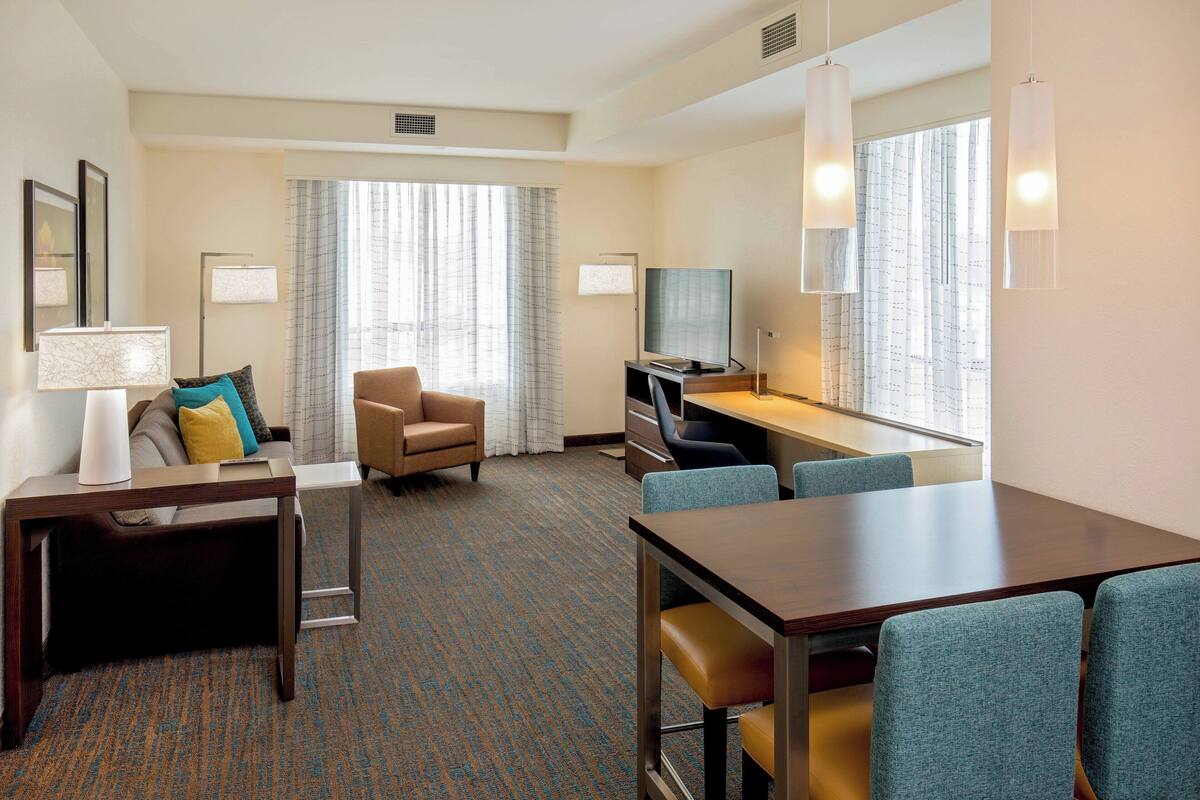 A hotel room with a sofa, a desk, a television, and a dining table with chairs.