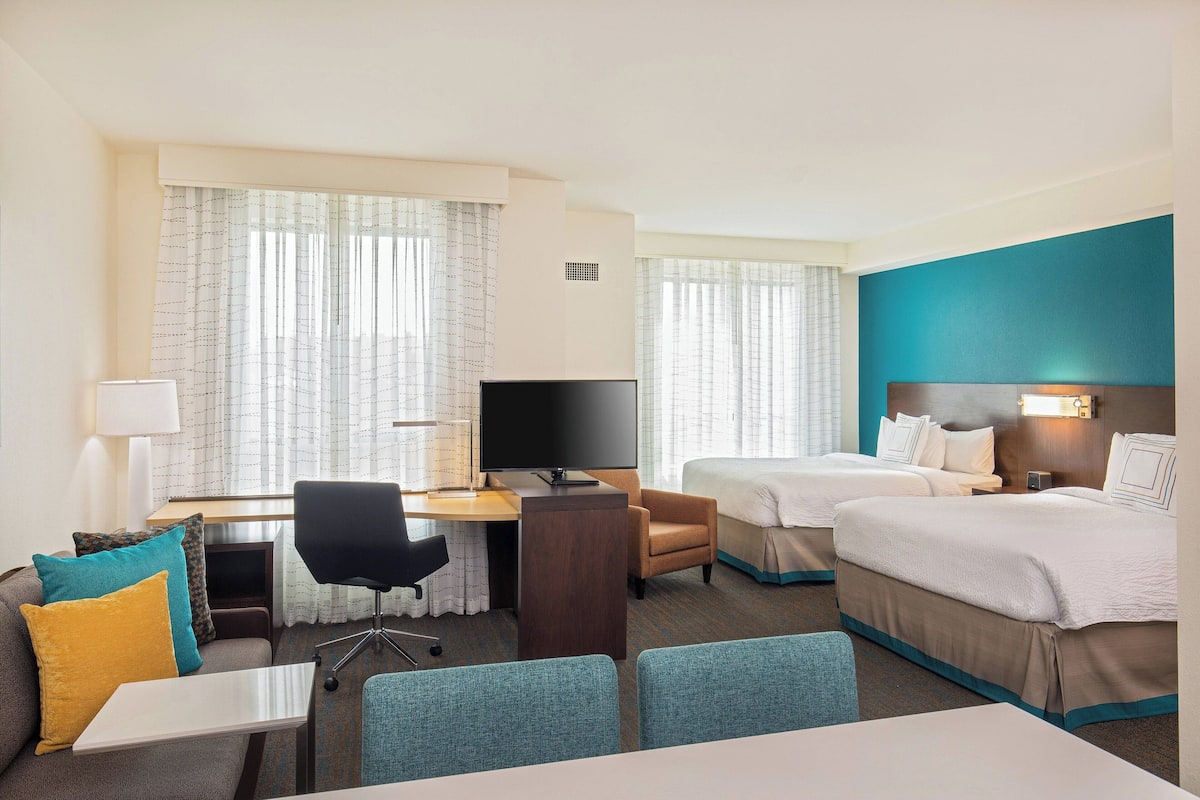 A hotel room with two beds, a desk with a computer, a chair, a small table, and a TV.