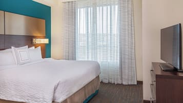 A hotel room with a large bed, a television on a wooden cabinet, and a window with sheer curtains.