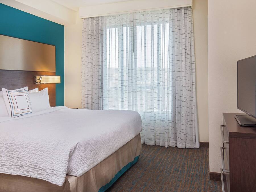 A hotel room with a large bed, a television on a wooden cabinet, and a window with sheer curtains.