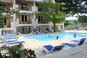 A pool area with lounge chairs and a view of a building with balconies. - Hôtel Restaurant L'Ermitage (Les Salles-sur-Verdon)