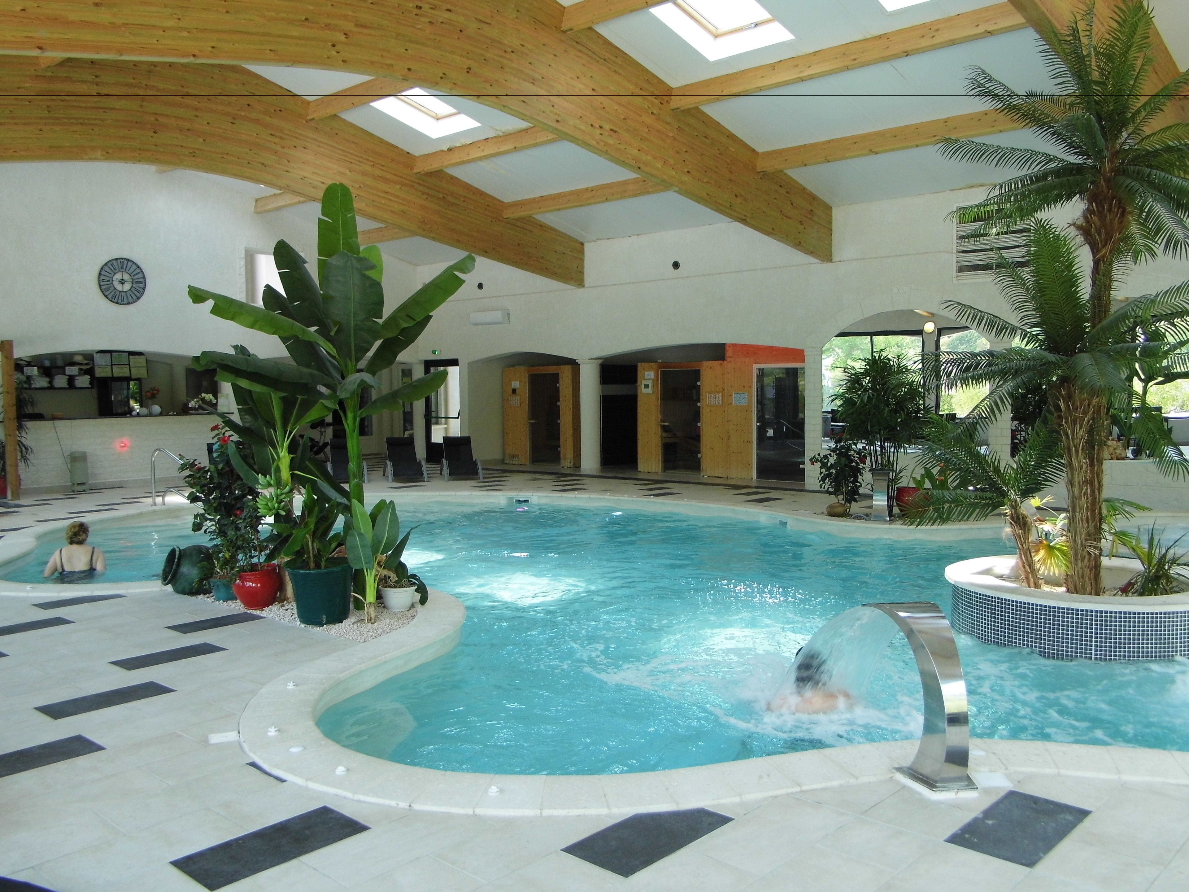 An indoor swimming pool with a wooden ceiling, a clock, and potted plants.