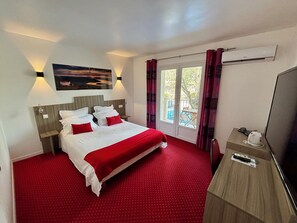A hotel room with a bed, a TV, a desk, and a window with curtains. - Hôtel Restaurant L'Ermitage (Les Salles-sur-Verdon)