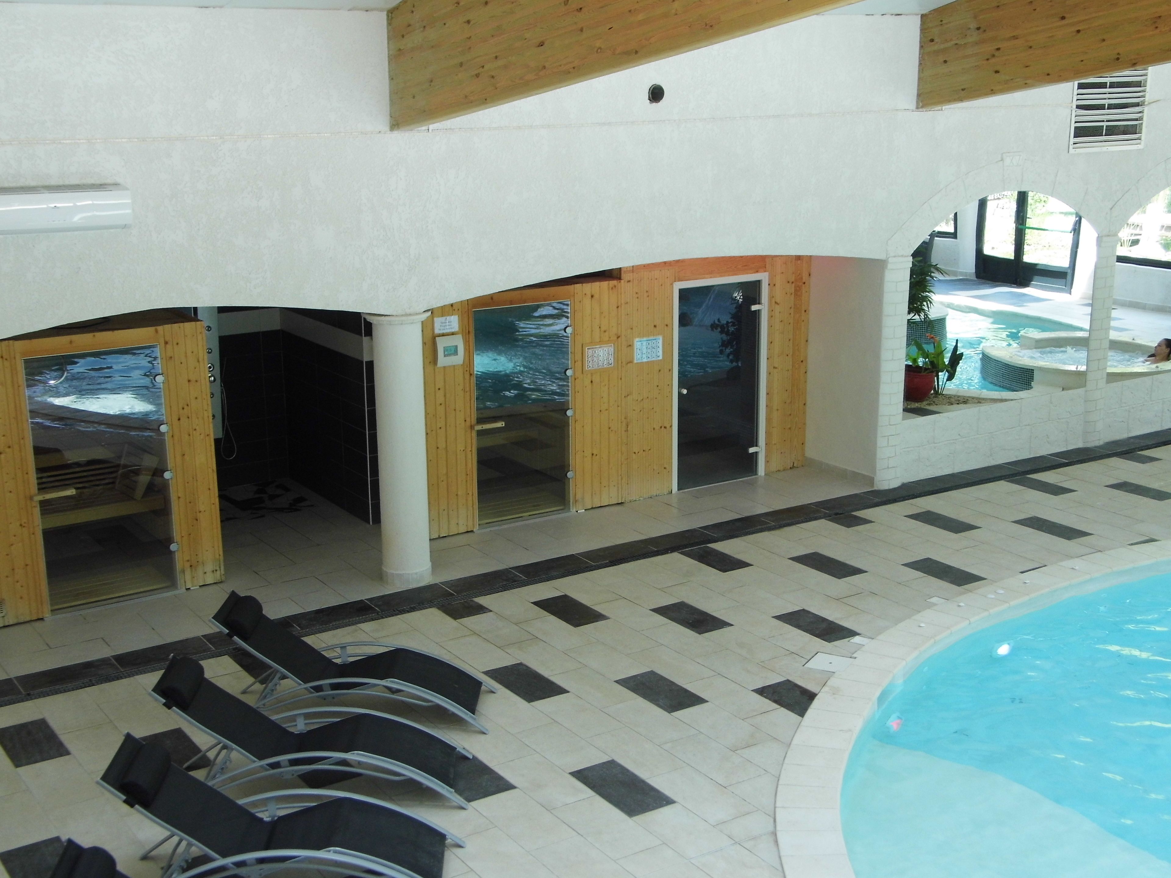 Un espace piscine doté de portes en bois donnant accès aux vestiaires, d’un sol carrelé et offrant une vue dégagée sur la piscine.