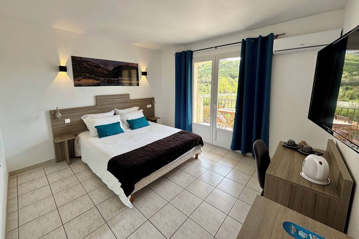 Ein modernes Hotelzimmer mit einem großen Bett, einem Schreibtisch mit Stuhl, einem Flachbildfernseher und einem Balkon mit Tisch und Stühlen.