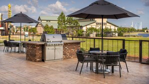 Een terras buiten met een barbecue, stoelen en parasols.
