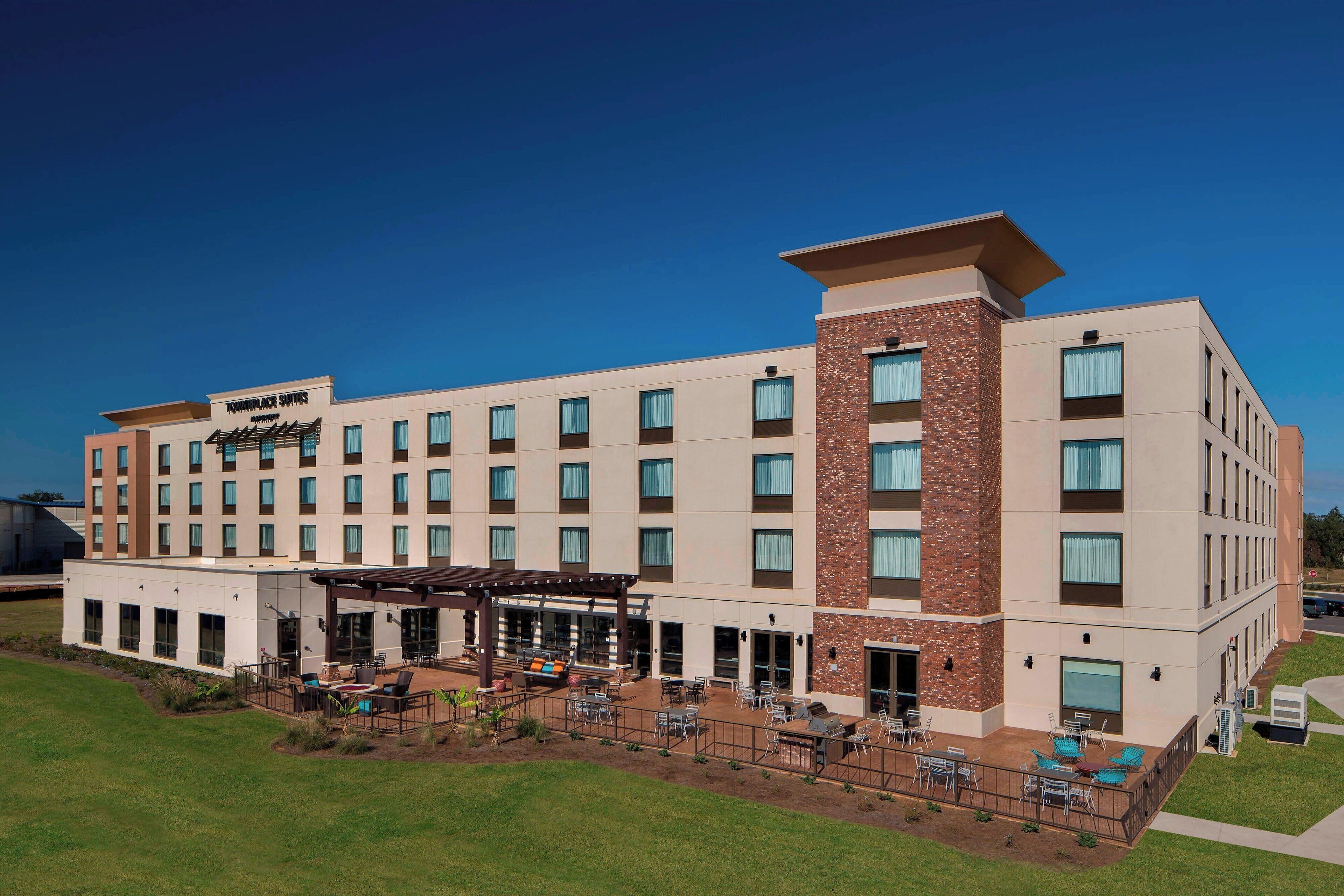 A hotel with a modern design, featuring multiple floors, a covered outdoor patio area, and a well-maintained lawn.