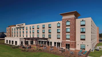 A hotel with a modern design, featuring multiple floors, a covered outdoor patio area, and a well-maintained lawn.