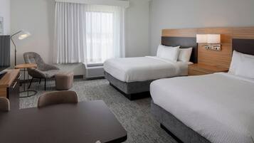 A hotel room with two beds, a desk, a chair, a lamp, and a window with curtains.