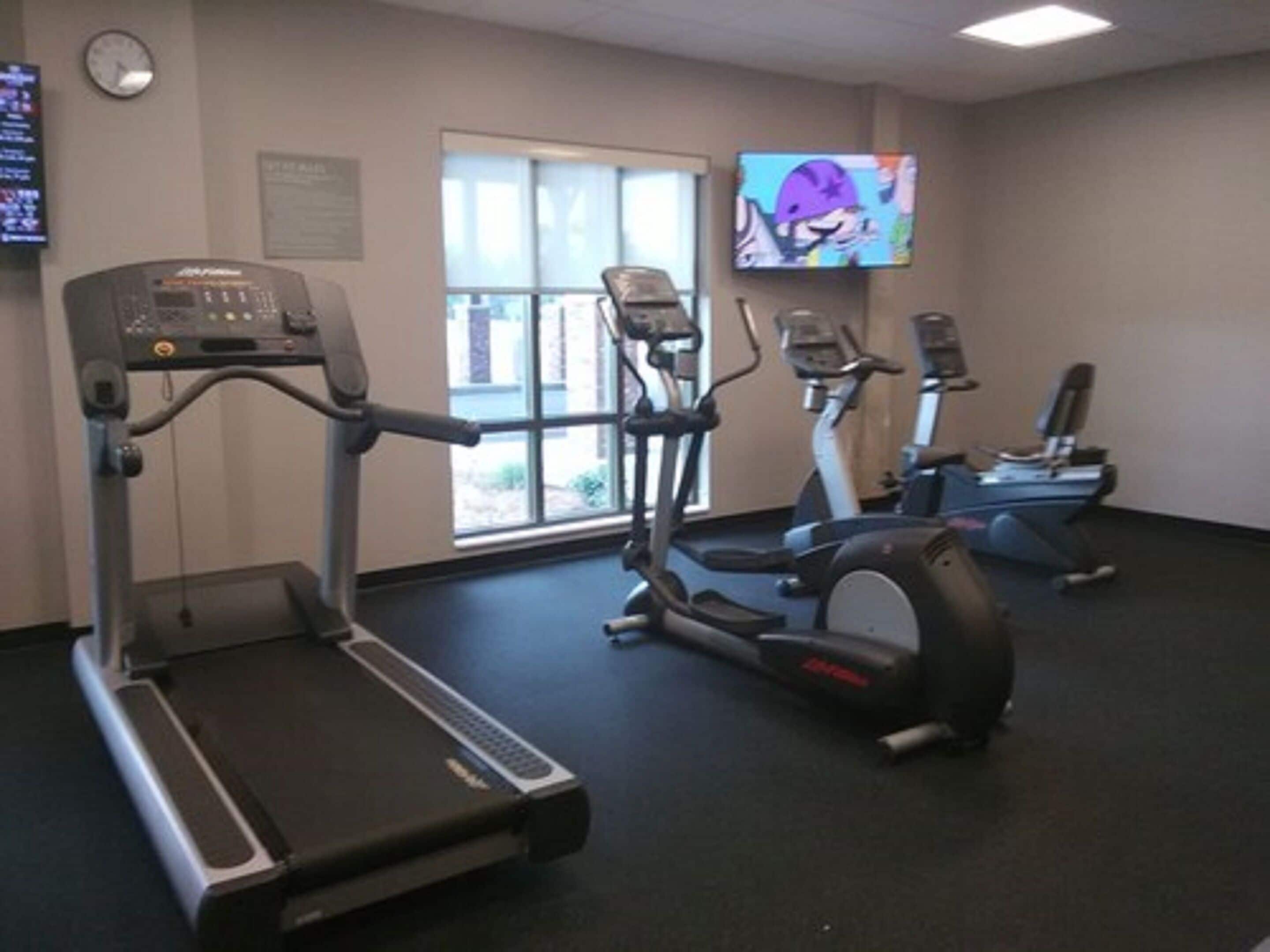Un gimnasio con cintas de correr, elípticas y un televisor en la pared.