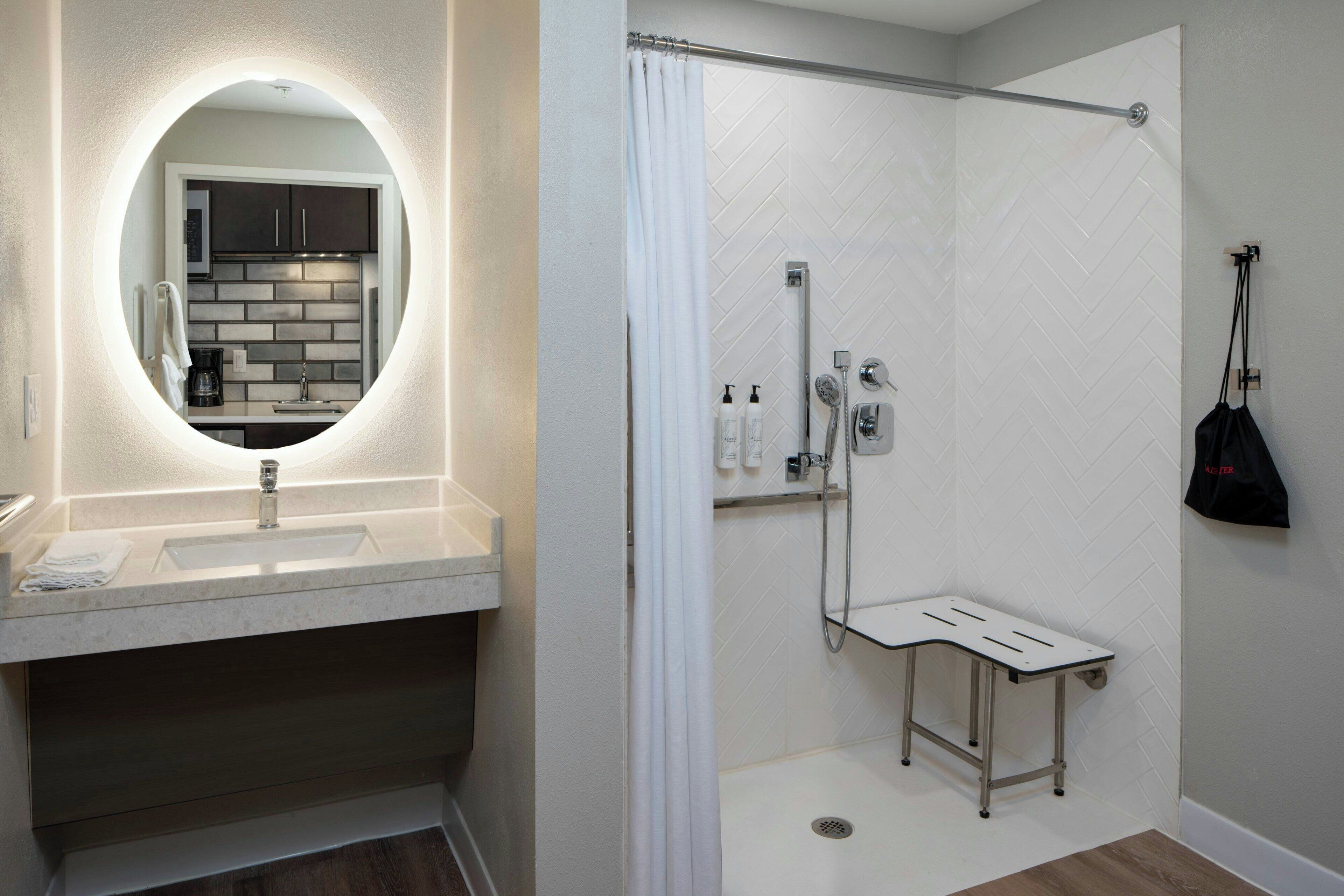A modern bathroom with a round mirror, a sink, and a shower area.