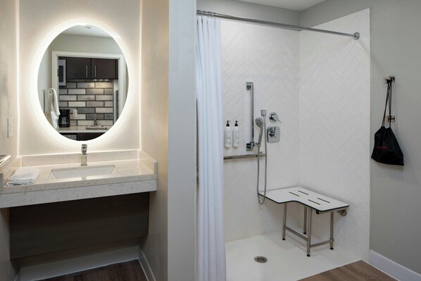 A modern bathroom with a round mirror, a sink, and a shower area. - TownePlace Suites by Marriott Foley at OWA (Foley)