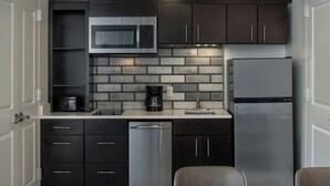Een moderne keuken met donkere kastjes, een RVS vaatwasser, een inbouwmagnetron en een koelkast.