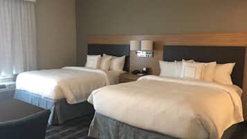 A hotel room with two beds, a desk, and a nightstand with a lamp.
