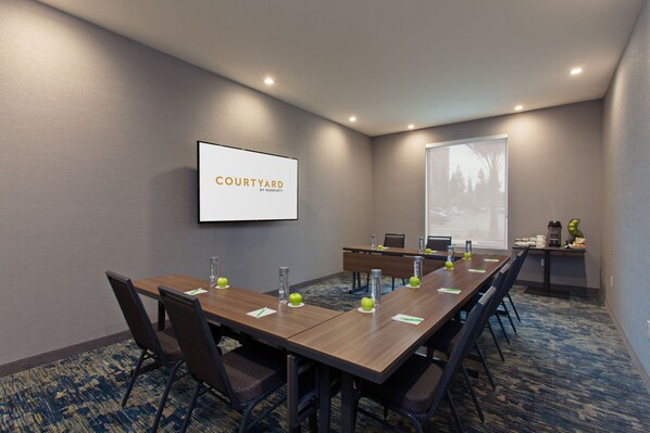 A conference room with a long table, chairs, a projector screen, and a screen displaying "Courtyard by Marriott".