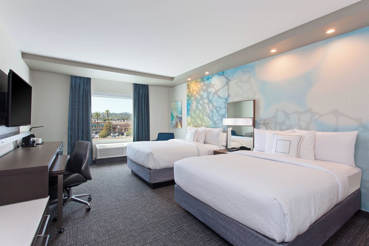 A hotel room with two beds, a desk, a chair, a TV, and a window with curtains.