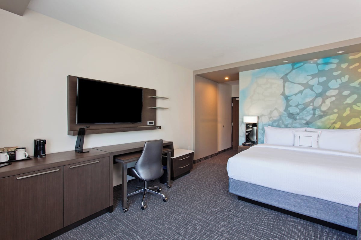 A hotel room with a bed, desk, chair, television, and a colorful wall mural.