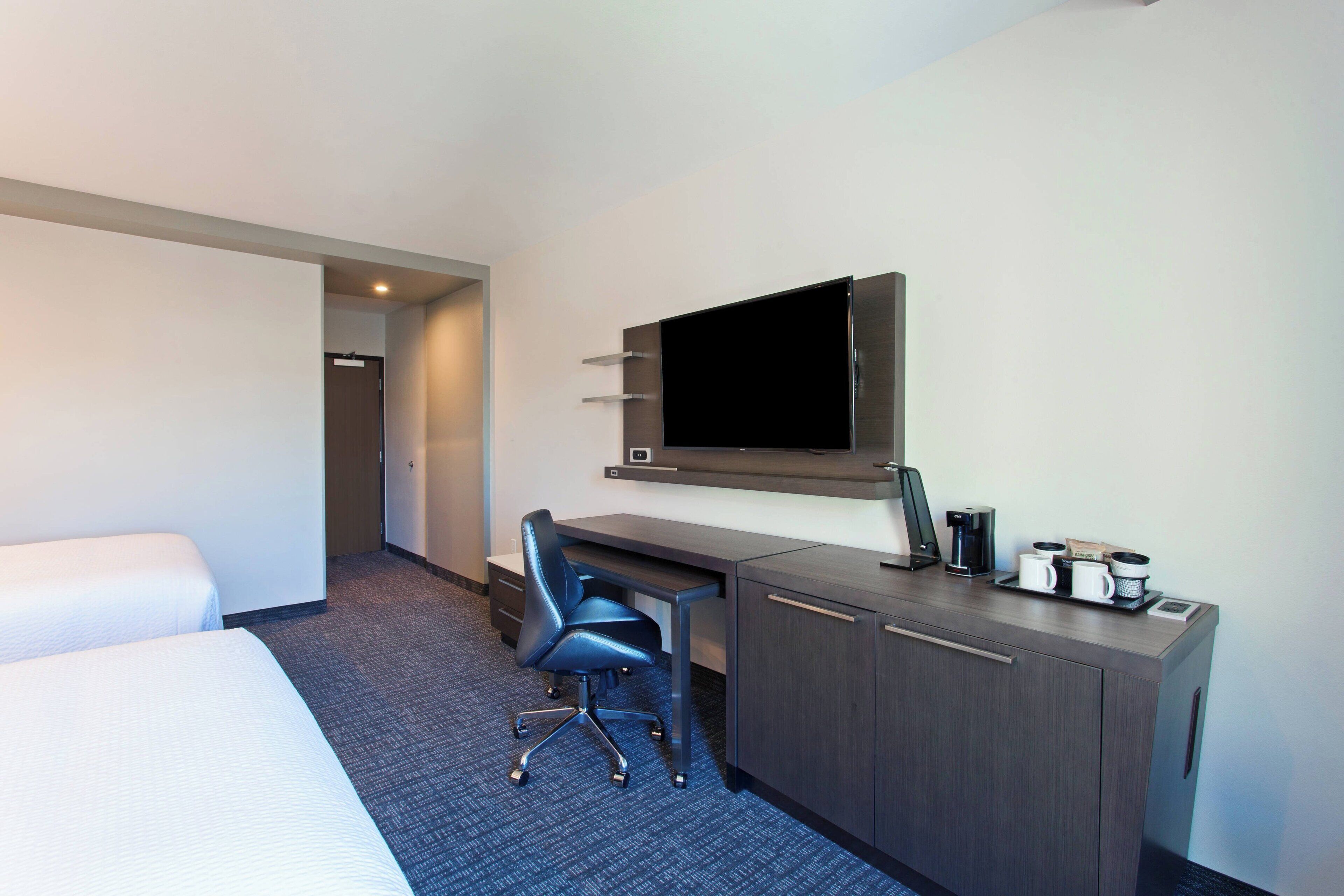 Une chambre d’hôtel comprenant un lit, un bureau avec une chaise, un téléviseur à écran plat et une machine à café.