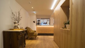 Un couloir doté d’un plancher en bois, d’une vieille commode, d’un fauteuil à rayures et d’un mur en bois sur lequel est fixée une étagère où est posée une plante.