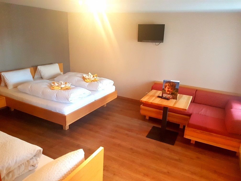 Una habitación de hotel con cama, una mesa de madera, un sofá rojo y un televisor en la pared.