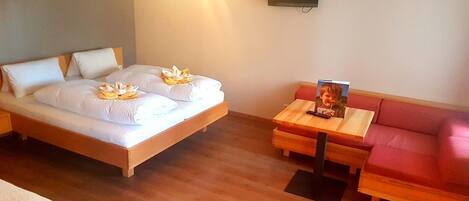 Una habitación de hotel con cama, una mesa de madera, un sofá rojo y un televisor en la pared.