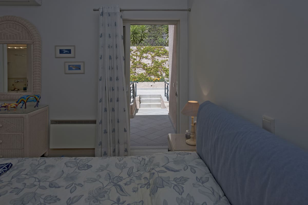A bedroom with a bed, a dresser, a mirror, and a door leading to a balcony.