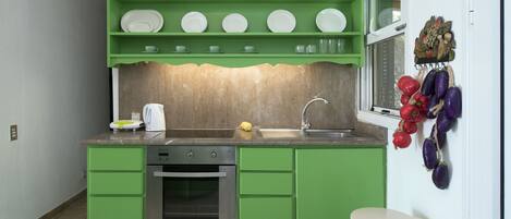 A kitchen with green cabinetry, a stainless steel oven, a sink, and a window with a view of the outside.