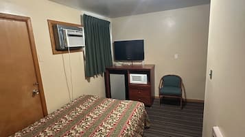 Een hotelkamer met een bed, een bureau met een televisie, een stoel en een plafondlamp.