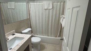 A bathroom with a sink, toilet, bathtub, and shower curtain. - Budget Inn (Cambridge)