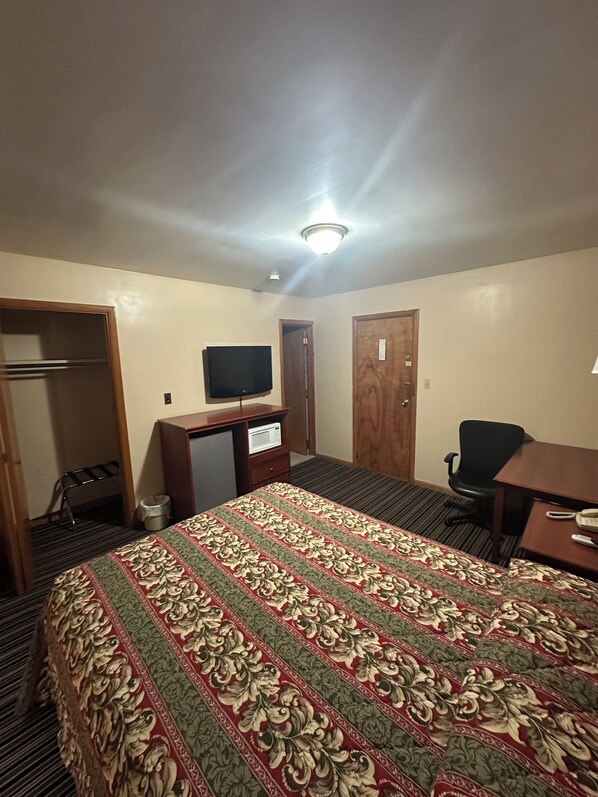 Una habitación de hotel con cama, escritorio, televisor, silla y armario.
