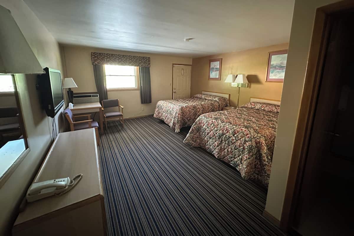 Quarto de hotel com duas camas, uma mesa de trabalho com telefone, televisão e janela com cortinas.
