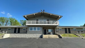 A two-story building with a balcony, a parking lot, and a stone wall. - Budget Inn (Cambridge)