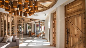 Un hall d’entrée spacieux au design moderne, comprenant un comptoir d’accueil en bois, un canapé et une grande porte en bois.