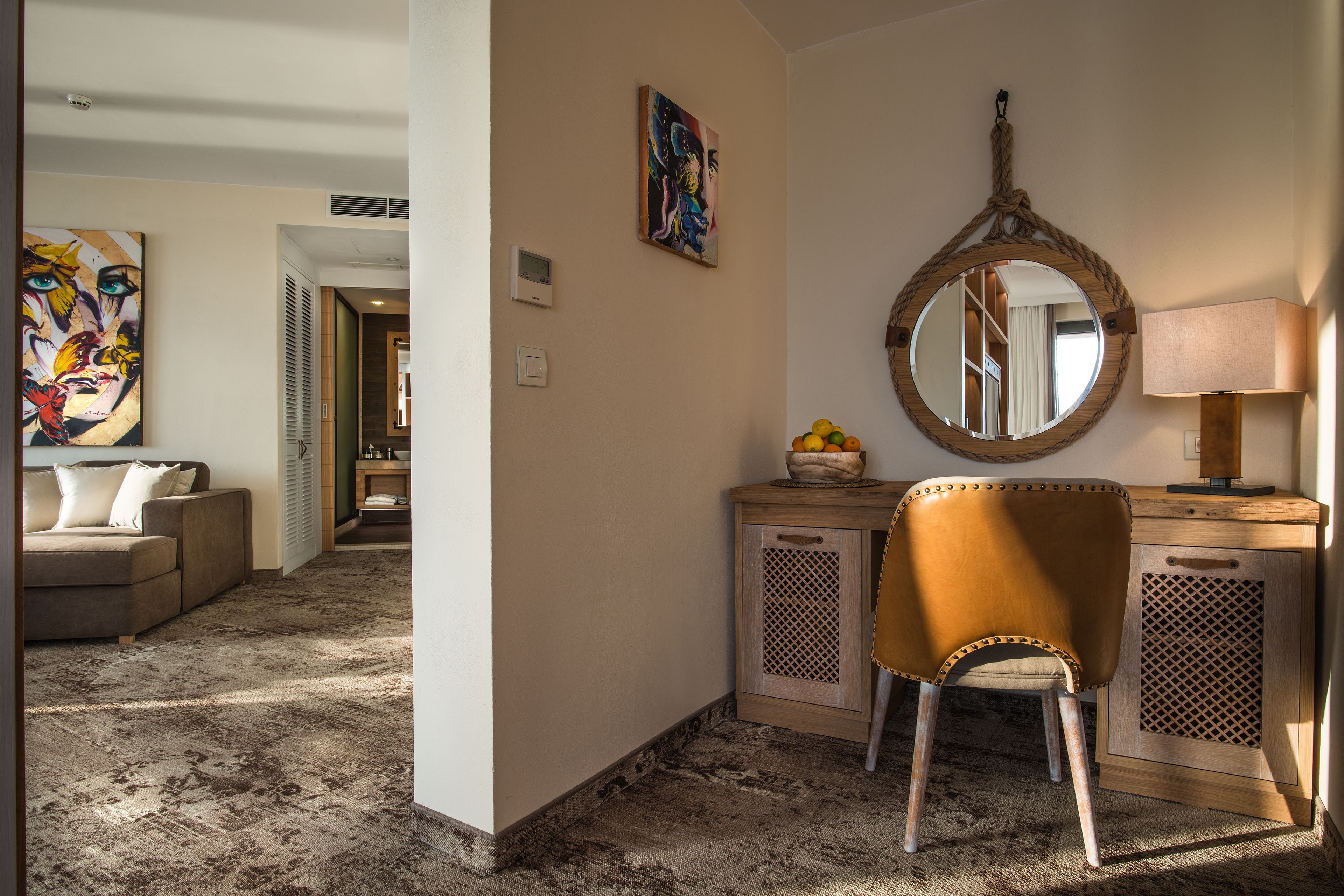 A hotel room with a sofa, a desk, a chair, a mirror, and a lamp.