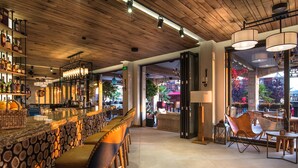 Un espace bar avec un plafond en bois, des tabourets de bar et un mur décoré d’un motif imitant des troncs d’arbres.