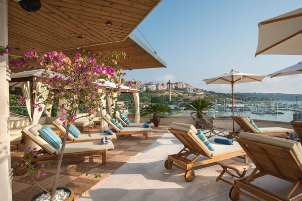 Un salon sur le toit avec des chaises longues, une pergola et une vue sur un port de plaisance.