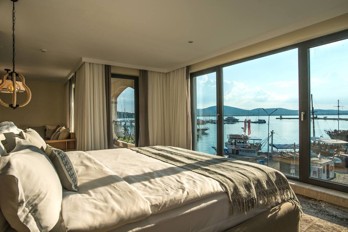 Ein Hotelzimmer mit einem großen Bett, Blick auf den Yachthafen und einer Hängelampe.