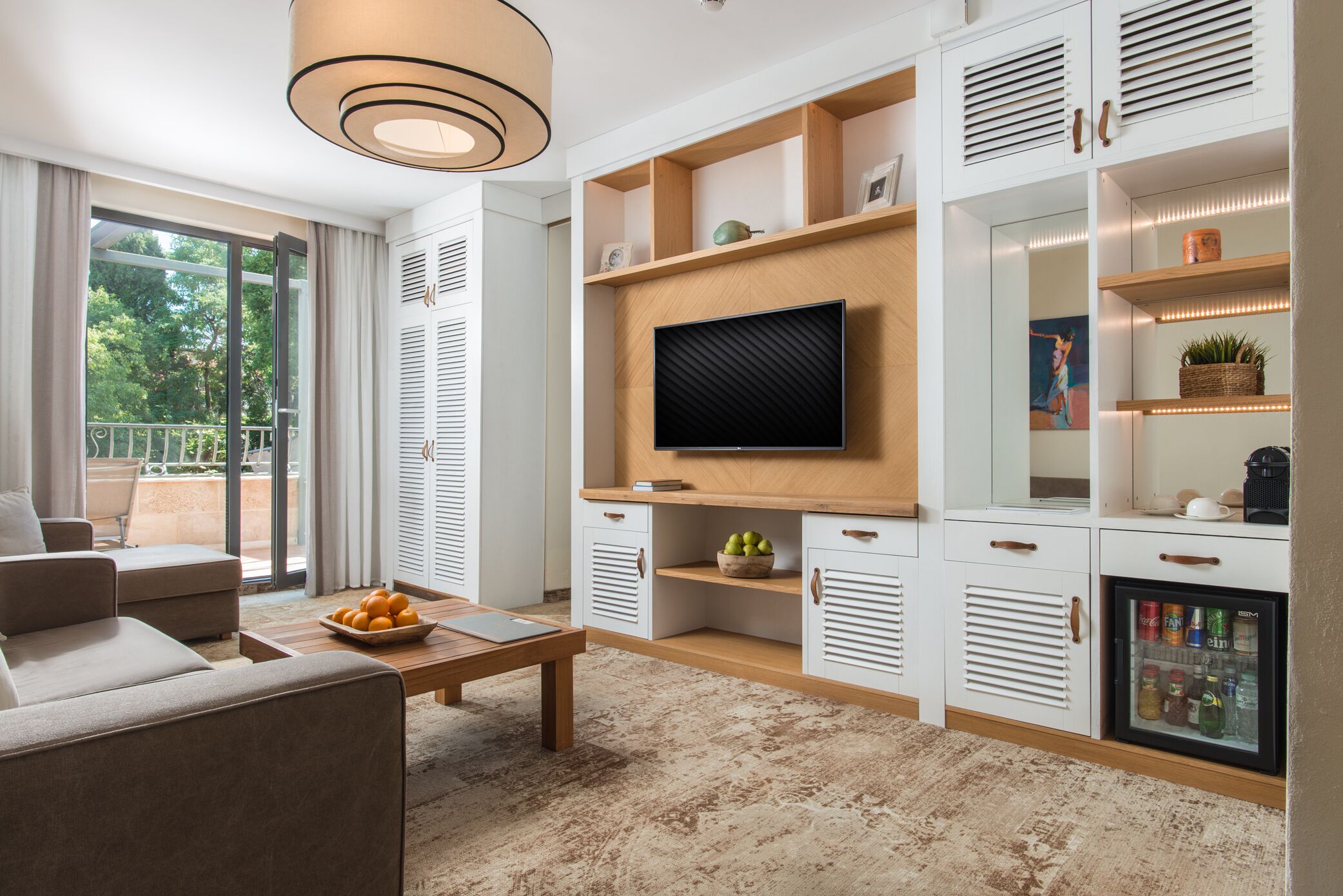 Una sala de estar moderna con un sofá, una mesa de centro y un televisor montado en una pared de madera. Hay un balcón con vistas a árboles.