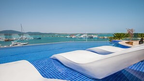 Une piscine bordée de chaises longues, offrant une vue sur les bateaux et une côte lointaine.